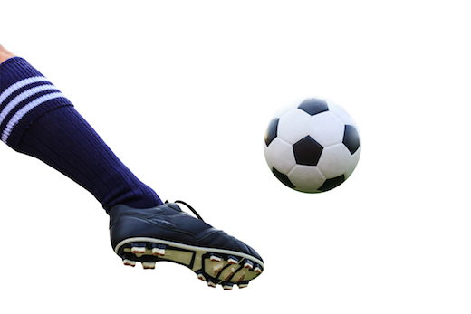 a leg in a shoe with cleats and a high blue sock kicking a soccer ball